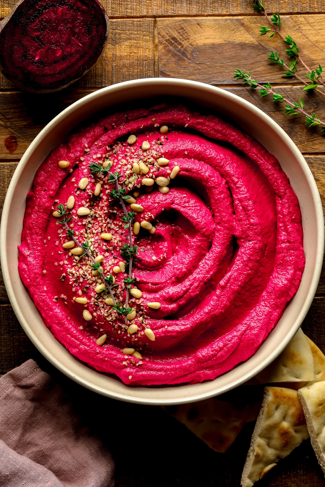 a bowl of pink beet hummus with pine nuts and thyme on top.