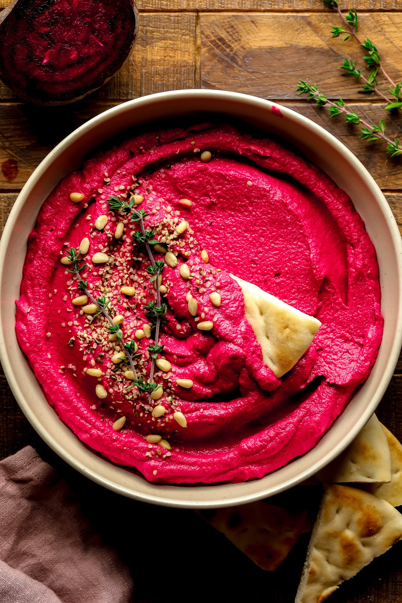 a bowl of pink beet hummus with pine nuts and thyme on top.