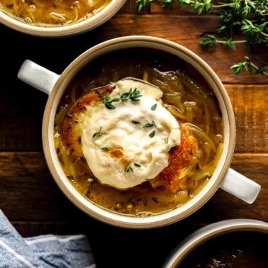 a bowl of Vegan French Onion Soup topped with toasted vegan cheesy bread.