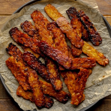 close up on a pile of pan-fried tempeh bacon slices.