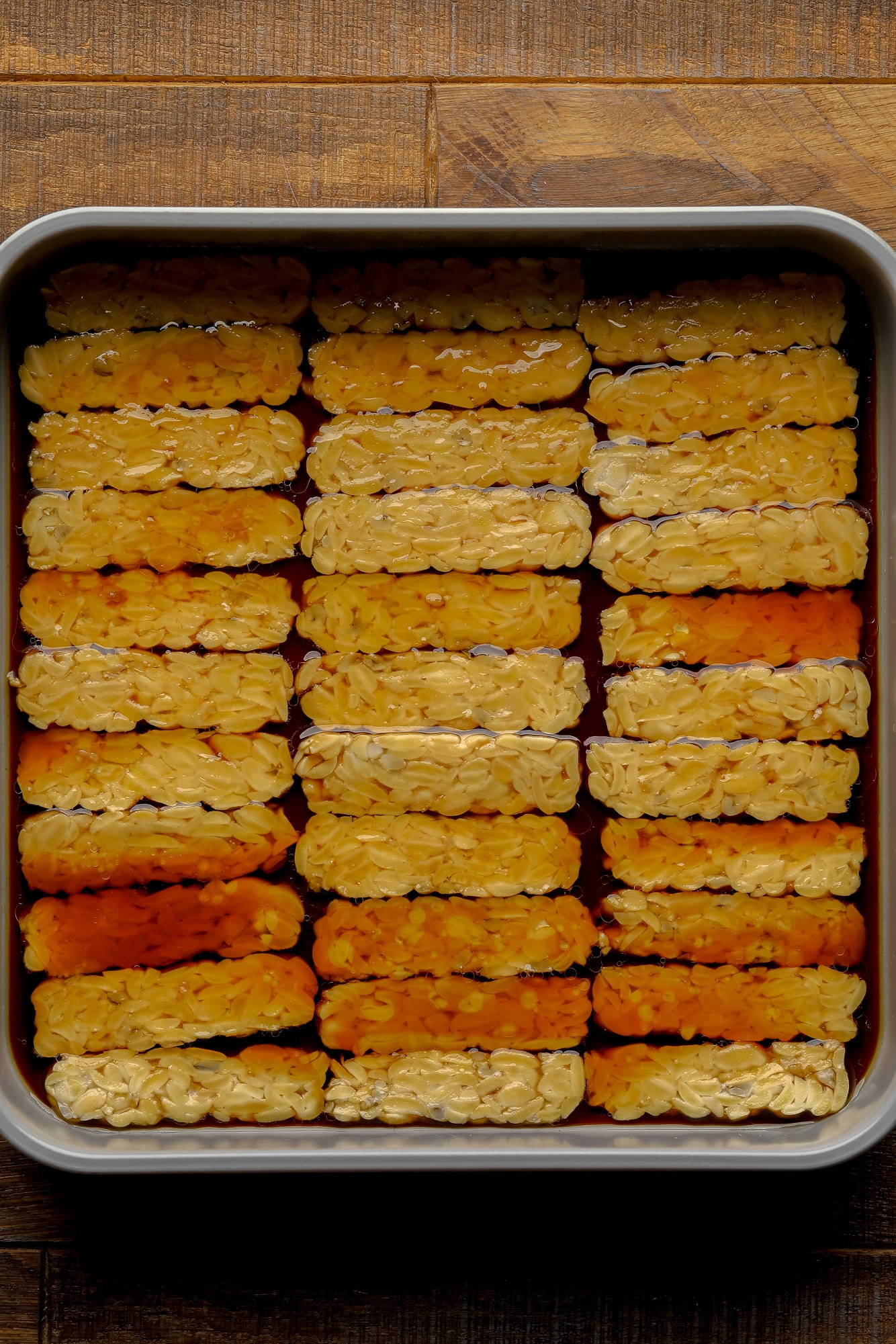 soaking tempeh slices in a brown marinade.