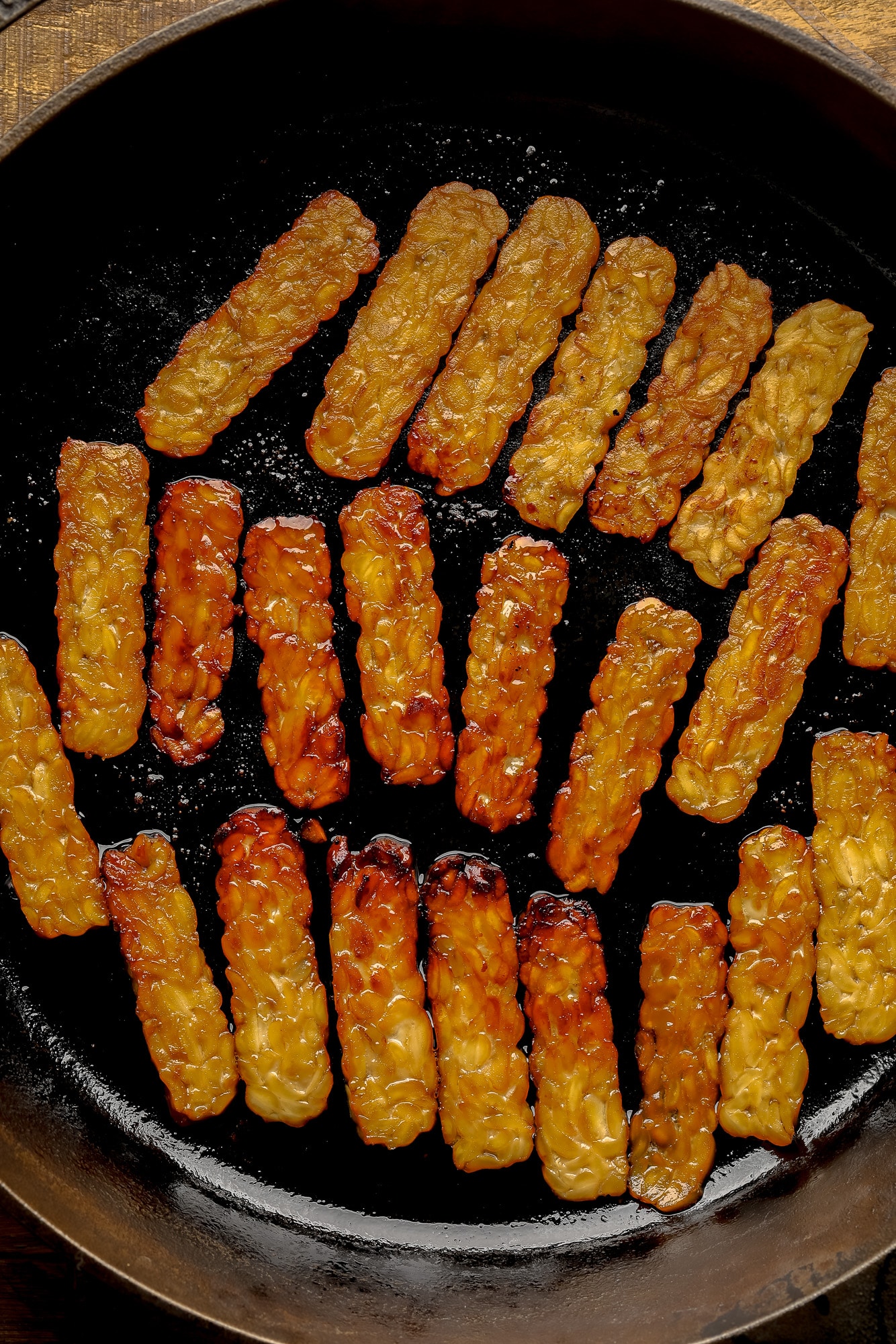 frying slices of tempeh bacon in a black skillet.