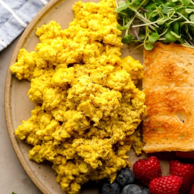 close up on a pile of yellow tofu scramble on a plate with toast, greens, and berries.