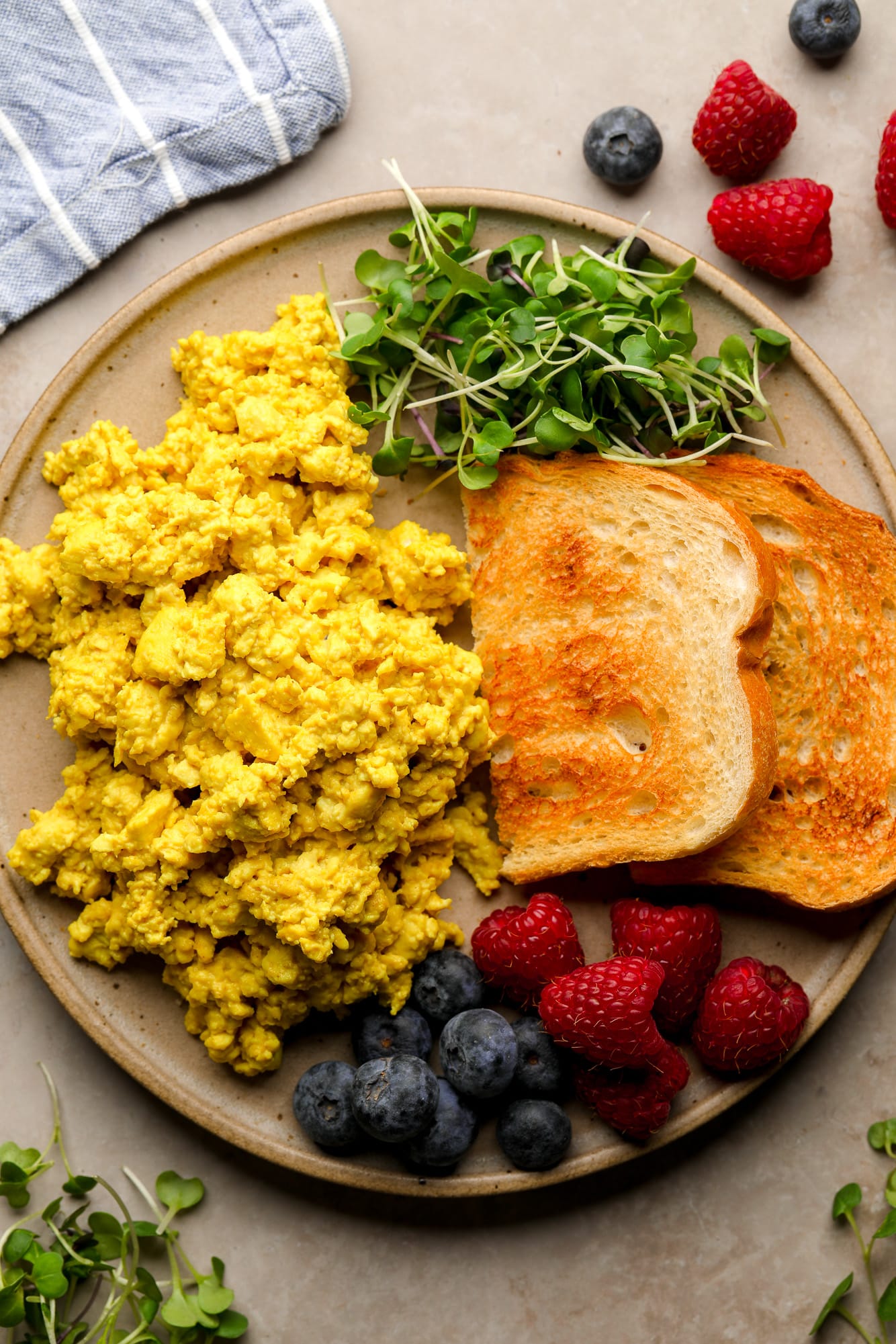 yellow tofu scramble on a plate with toast, greens, and berries.