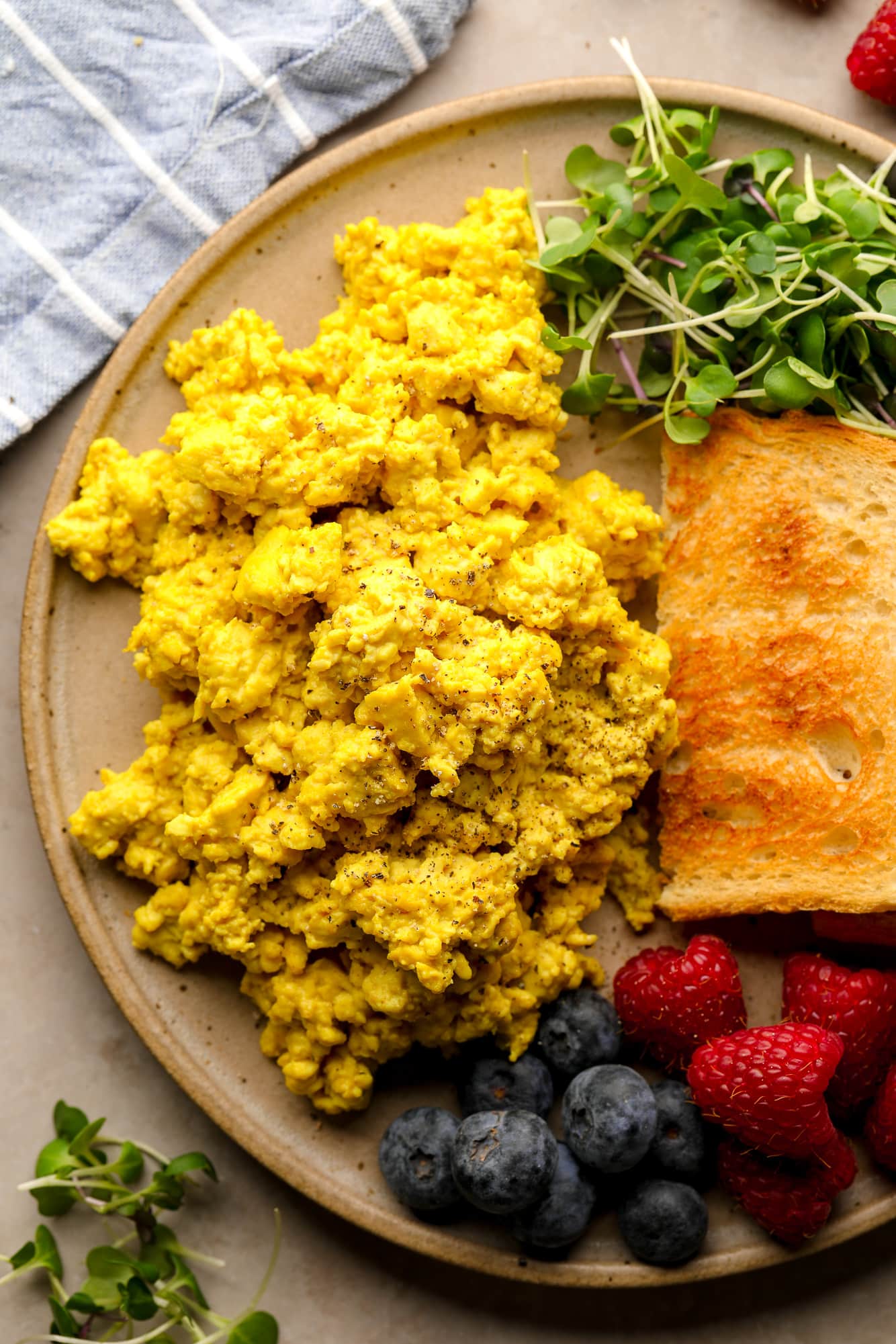 yellow tofu scramble on a plate with toast, greens, and berries.