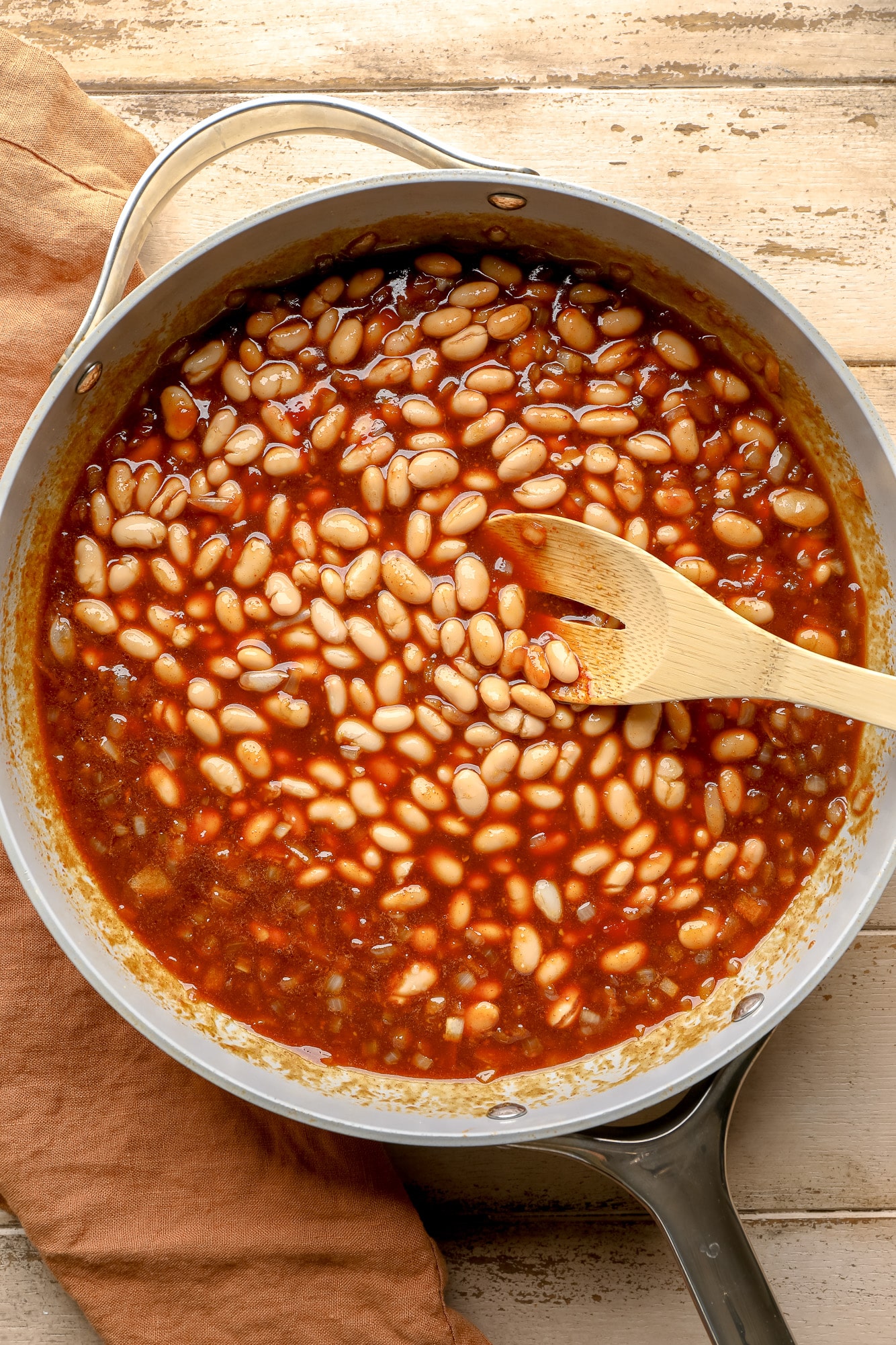 using a wooden spoon to stir white beans into a baked bean sauce.