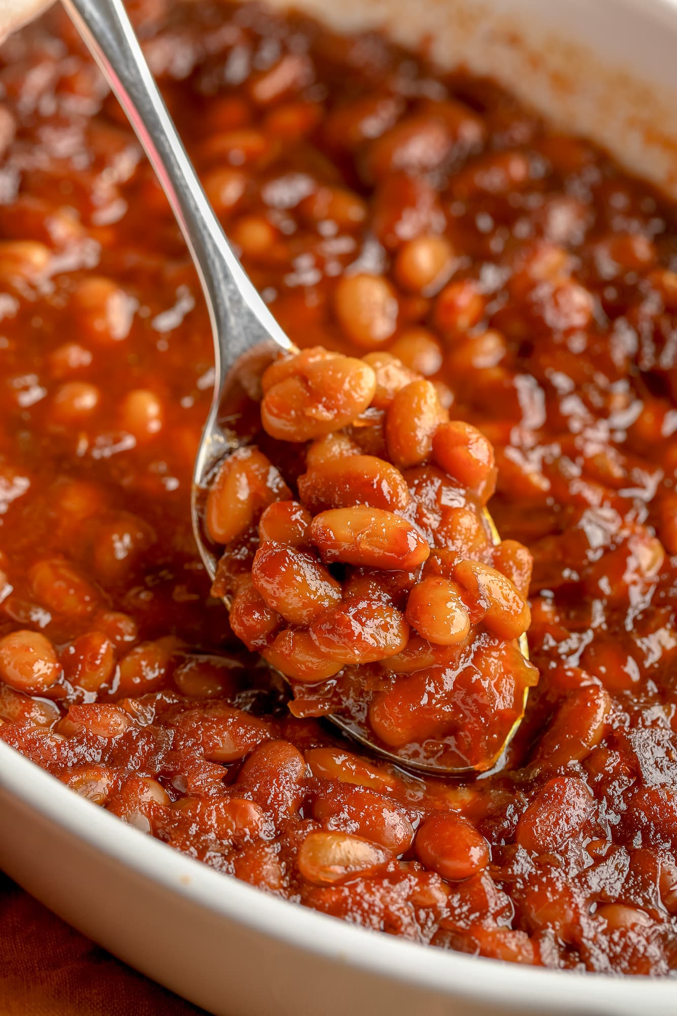 close up on a spoon scooping up a bite of vegan baked beans from a casserole dish.