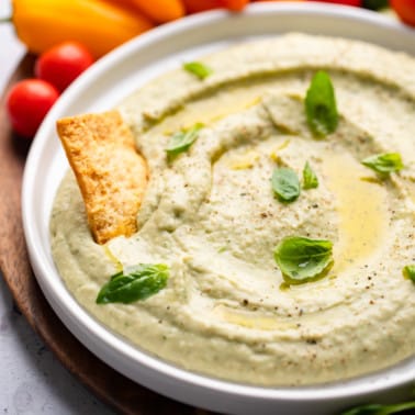 close up on white bean dip in a white bowl with a cracker pushed in the dip.