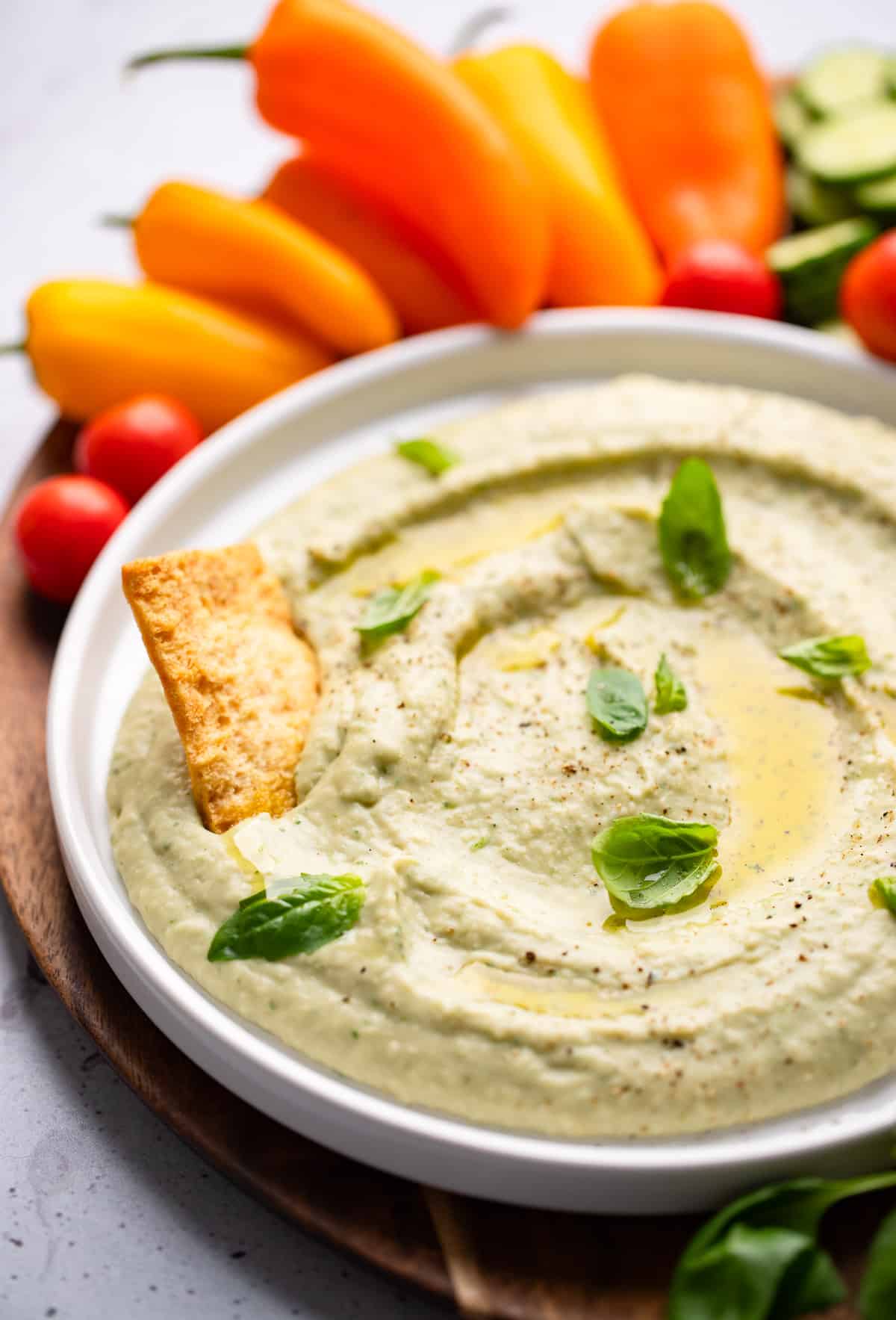 close up on white bean dip in a white bowl with a cracker pushed in the dip.