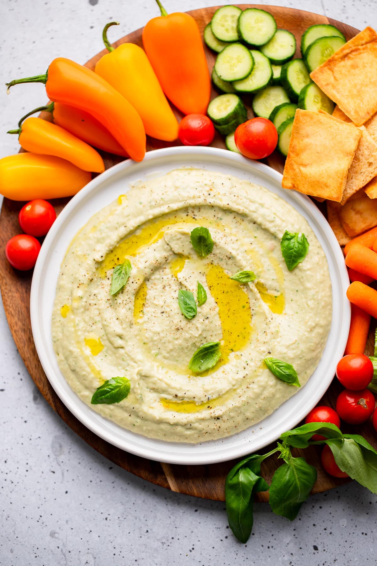 white bean dip in a white bowl surrounded by vegetables and crackers.