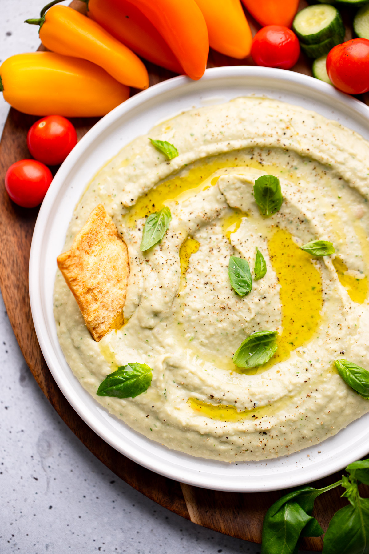 close up on white bean dip in a white bowl surrounded by vegetables and crackers.