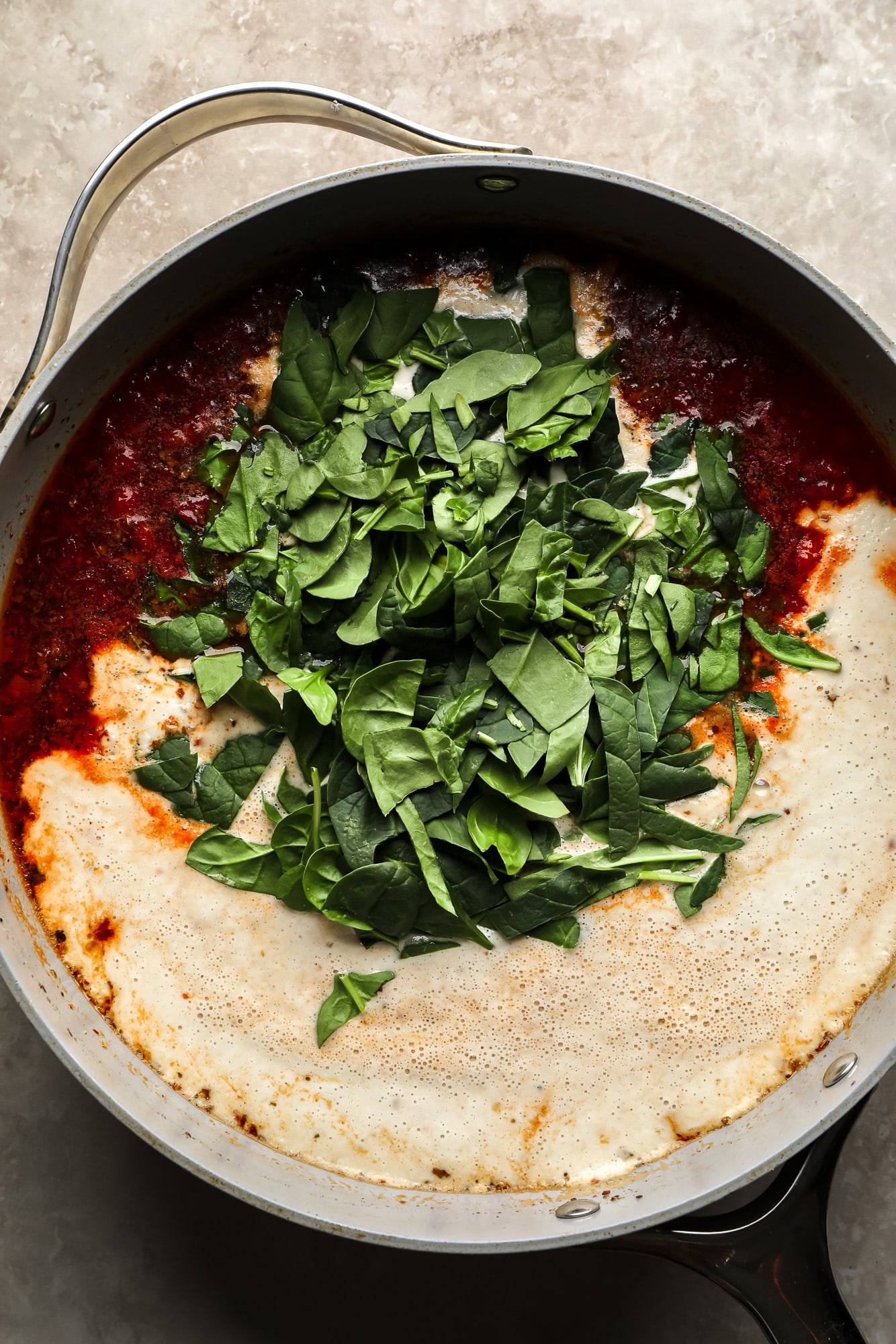 adding spinach to the sauce for marry me tofu in a large skillet.