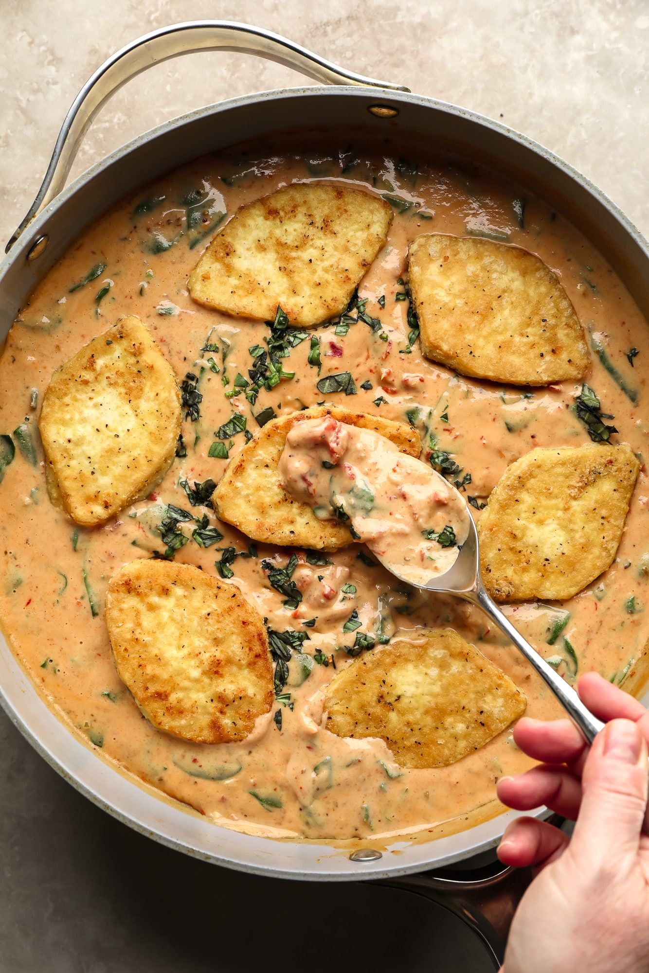 womans hand spooning marry me tofu sauce over a piece of fried tofu in a skillet.