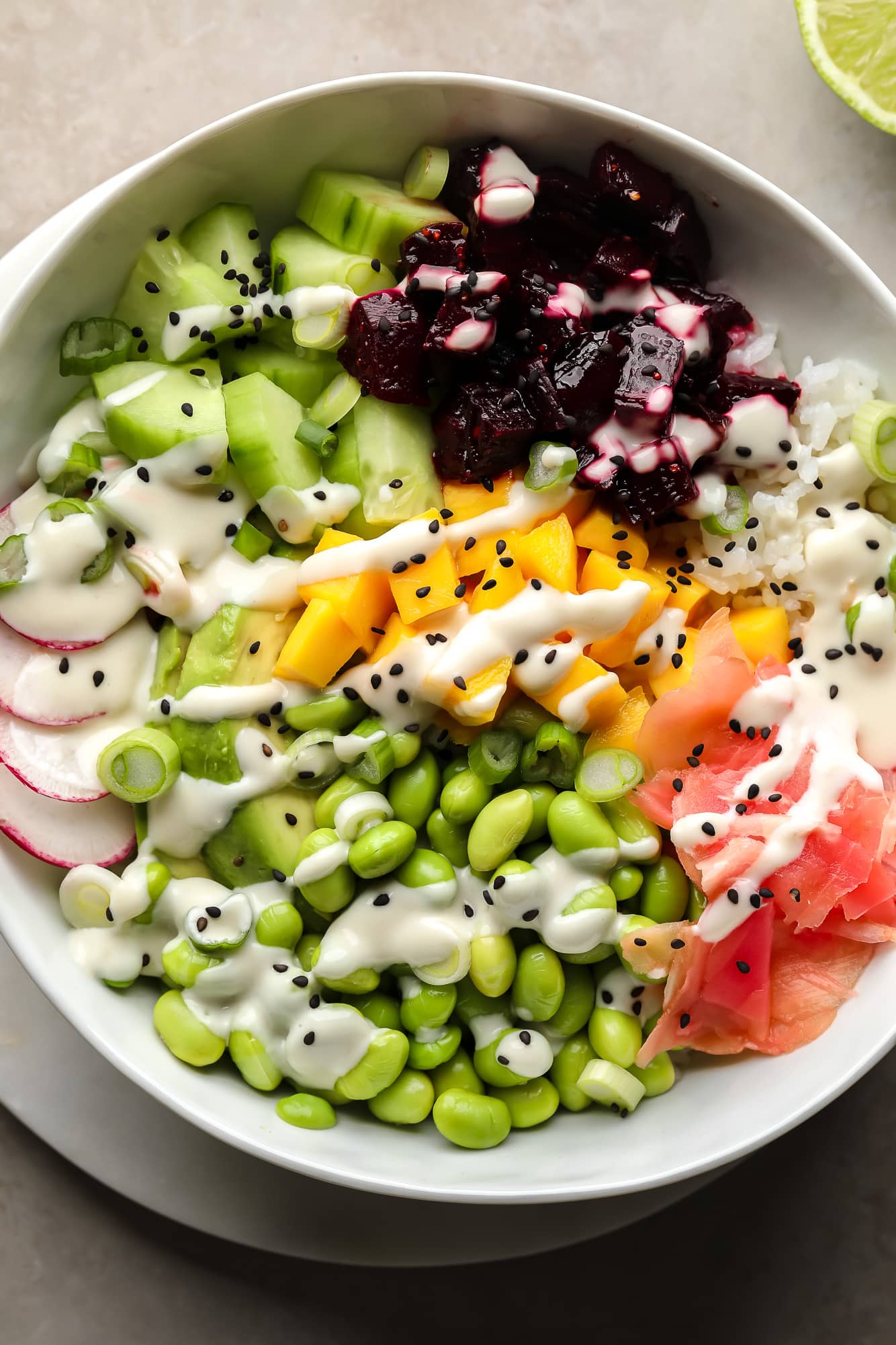 A beet poke bowl topped with marinated beets, mango, radishes, edamame, cucumber, pickled ginger, and wasabi mayo.