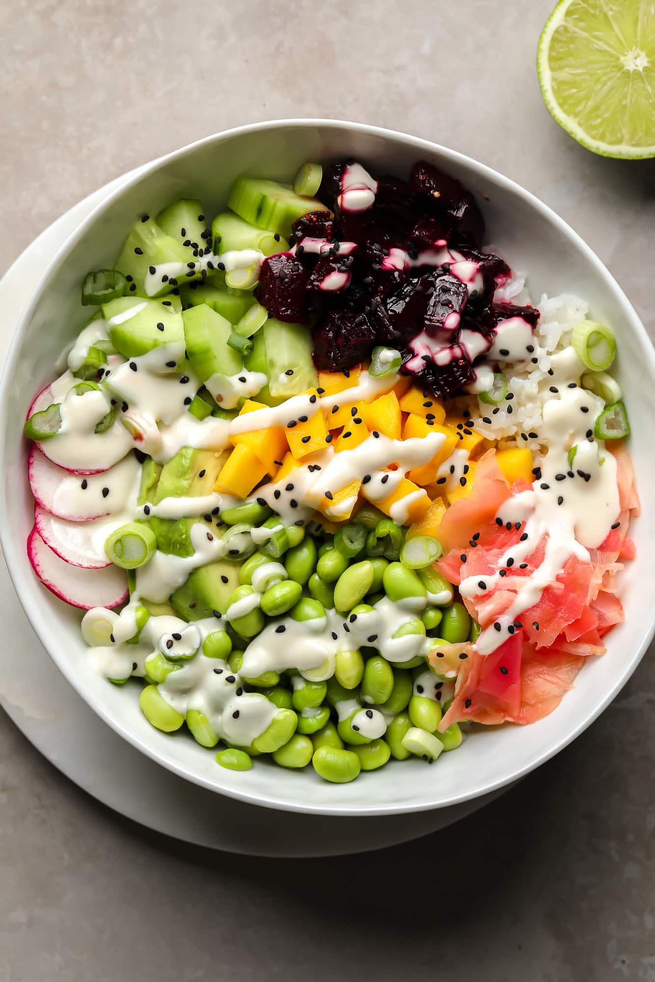 A beet poke bowl topped with marinated beets, mango, radishes, edamame, cucumber, pickled ginger, and wasabi mayo.